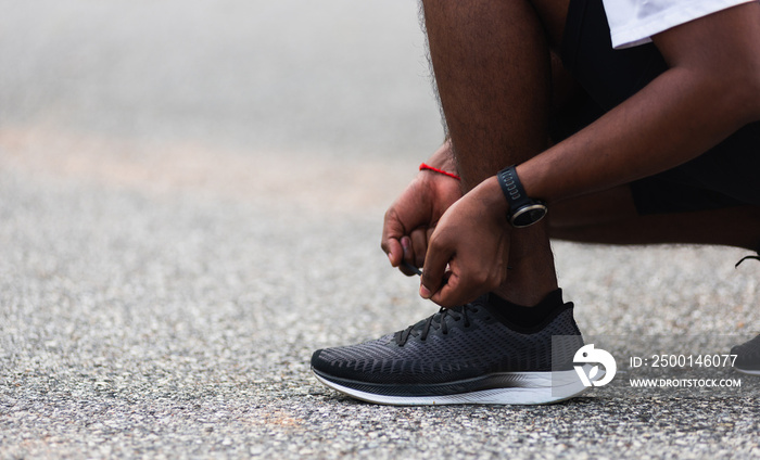 Close up Asian sport runner black man wear watch sitting he trying shoelace running shoes getting ready for jogging and run at the outdoor street health park, healthy exercise workout concept