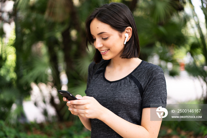 Young sport caucasian woman sending a message or email with the mobile at outdoors in a park