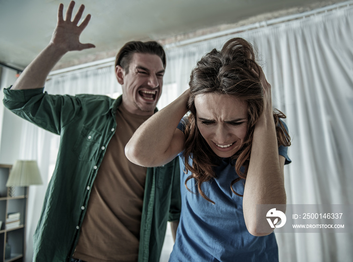 Terrified woman is covering her head while cruel man is going to hit her. Family violence concept