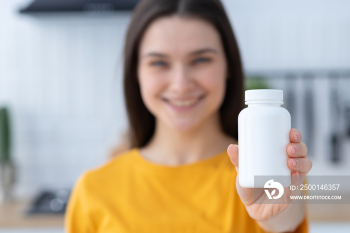 Happy young Caucasian woman holding bottle of dietary supplements or vitamins in her hands. Close up. Healthy lifestyle concept