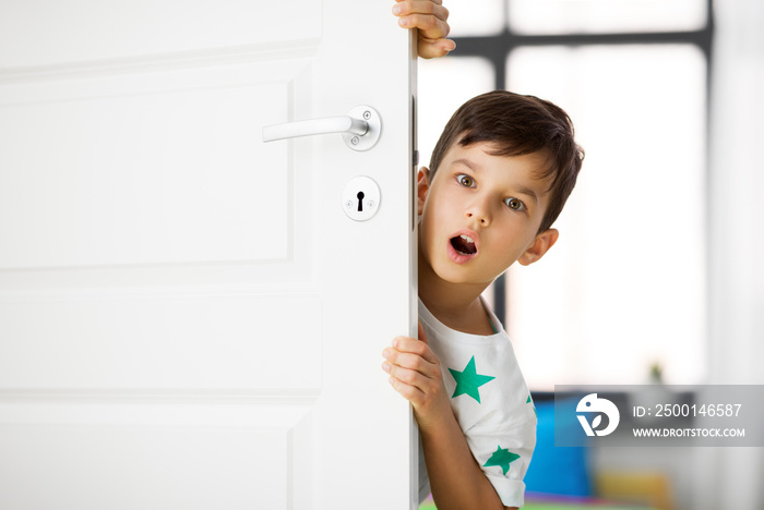 childhood, emotions and people concept - surprised little boy behind door at home