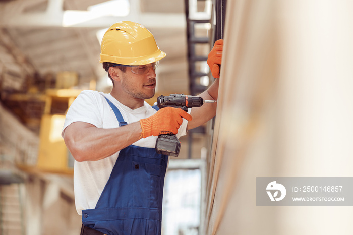 Male worker using cordless electric drill at construction site