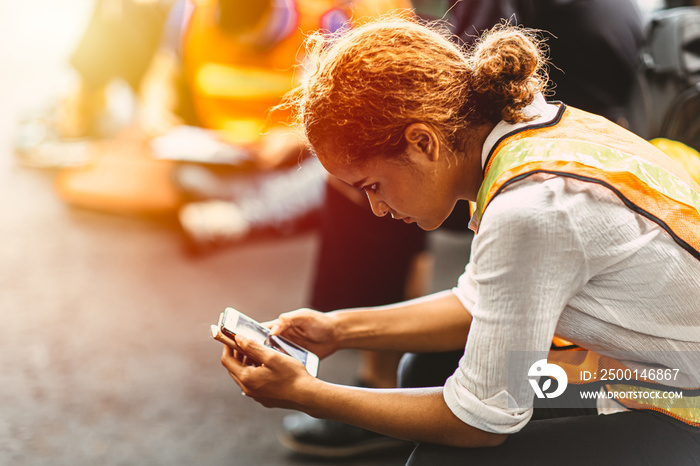 Black African American woman break relaxes and reads the news on her mobile smart phone in an industrial factory.