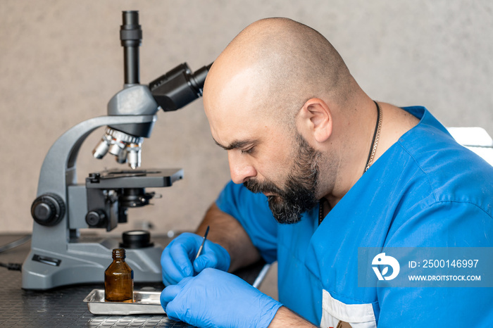 Male laboratory assistant examining biomaterial samples in a microscope