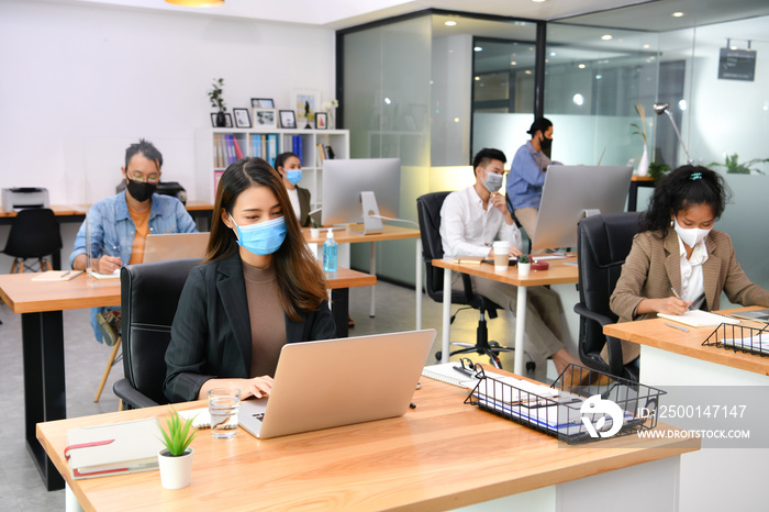 Asian office workers wearing face masks working in new normal office and doing social distancing during corona virus covid-19 pandemic