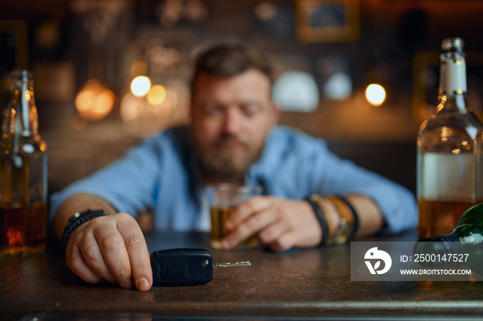 Drunk man with car key sitting at counter in bar