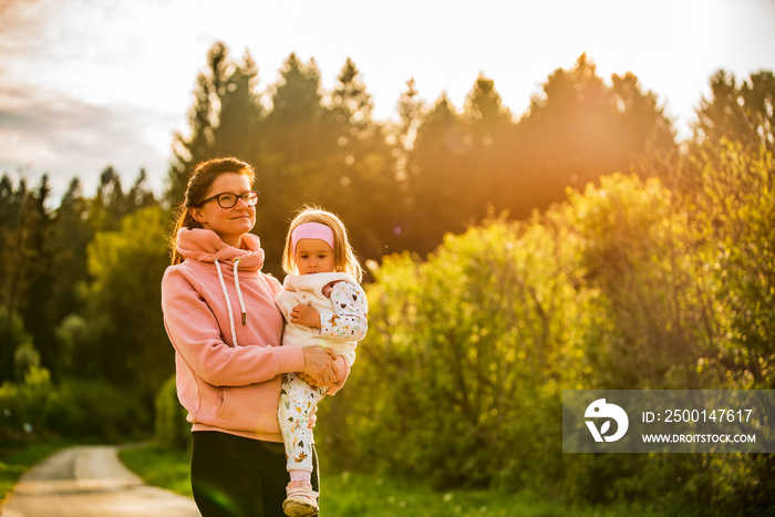 Mother and child walking on countryside road between agricultural fields towards vilage from forest