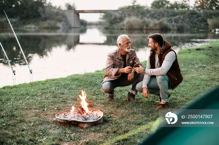 Happy senior father toasting with his son during their camping day in nature.