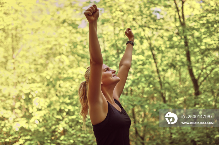 Woman raising her arms in triumph after a forest run