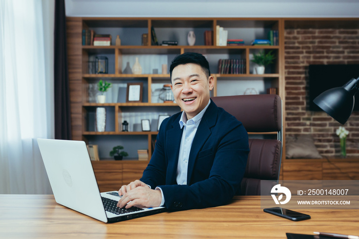Portrait of a successful Asian businessman in a classic office working on a laptop, smiling