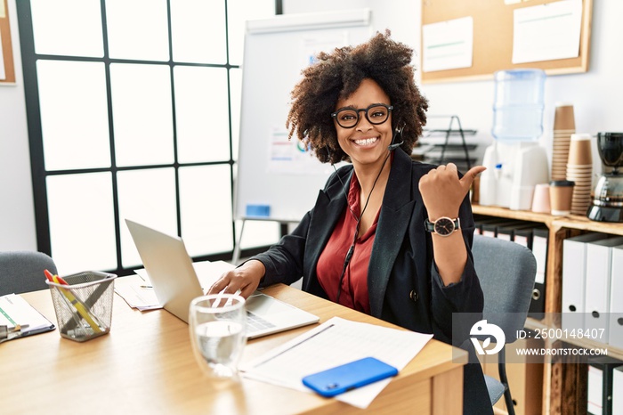 African american woman with afro hair working at the office wearing operator headset pointing to the back behind with hand and thumbs up, smiling confident