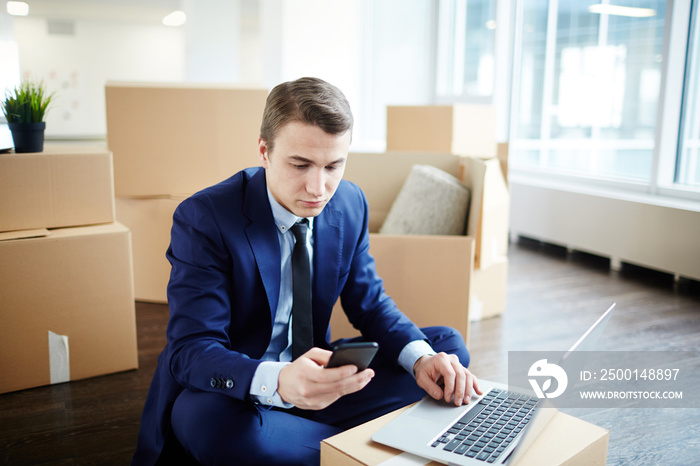 Young businessman texting in smartphone while ordering food online after relocation to new office