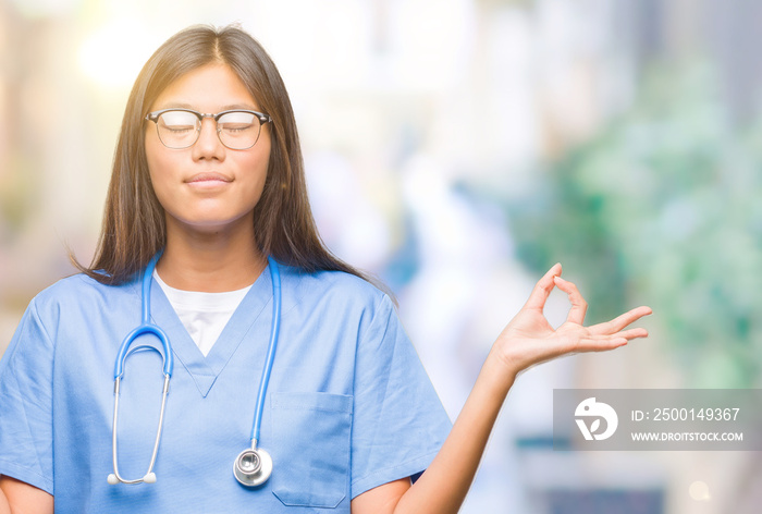 Young asian doctor woman over isolated background relax and smiling with eyes closed doing meditation gesture with fingers. Yoga concept.