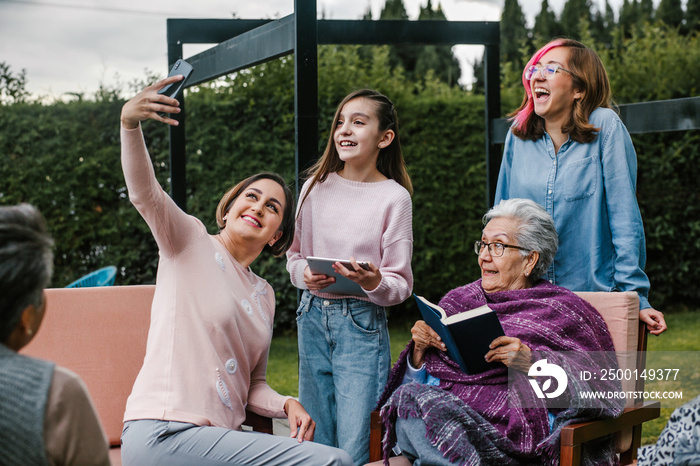 Hispanic women family reading a book and taking a photo selfie in a backyard outside home in Mexico city