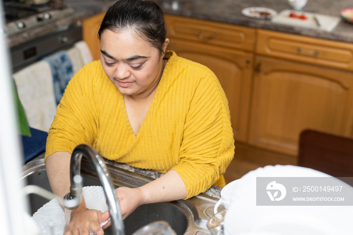 Young woman with down syndrome washing dishes at home