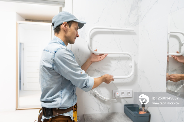 Plumber in medical mask installs electric heated towel rail in bathroom.