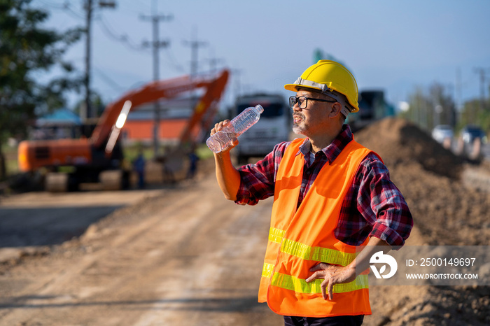 The foreman wears a safety vest and helmet. Take care of the workers and road construction machines at the job site, take a break and drink water.