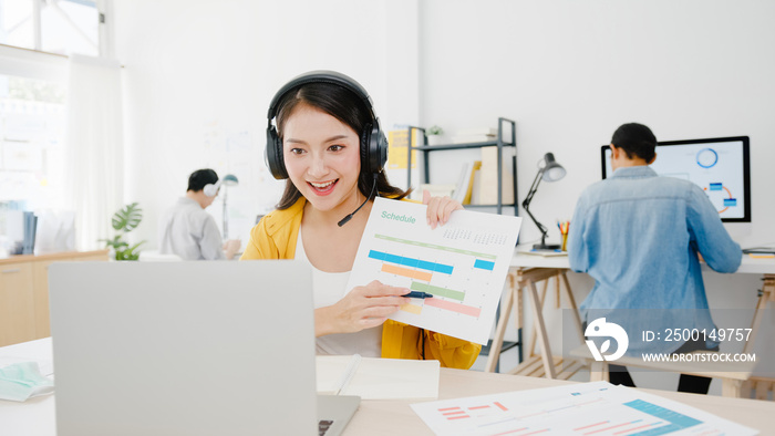 Asia businesswoman social distancing in new normal situation for virus prevention while using laptop presentation to colleagues about plan in video call while work in office. Life after corona virus.