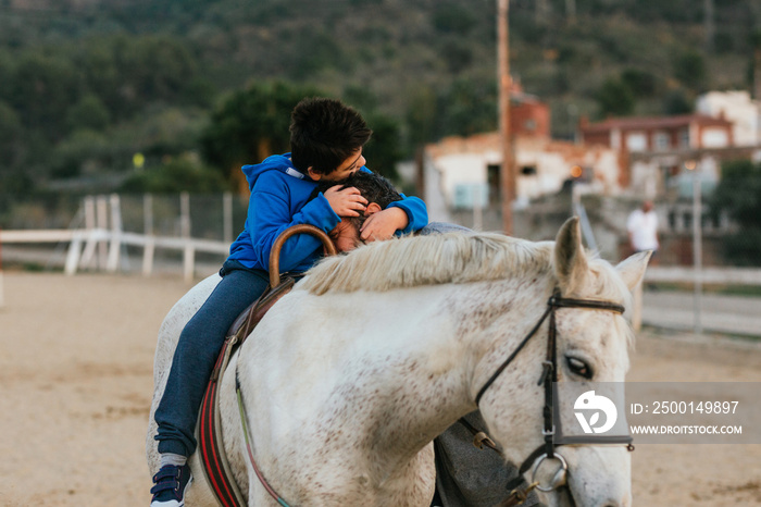 Boy with disabilities sitting on a horse while embracing his equine therapy instructor.