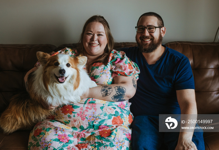 a couple sits on the couch holding their dog