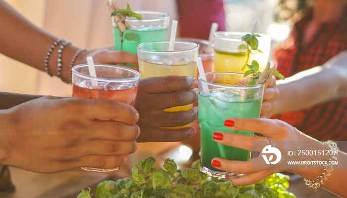 Happy people cheering with mojito and having fun - Multiracial friends drinking coktails in a beach bar outside in summer days with face mask on to be protected from coronavirus