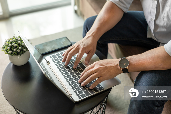 businessman sitting on sofa with mobile phone using laptop working at home to send and send reply to email Message customer service