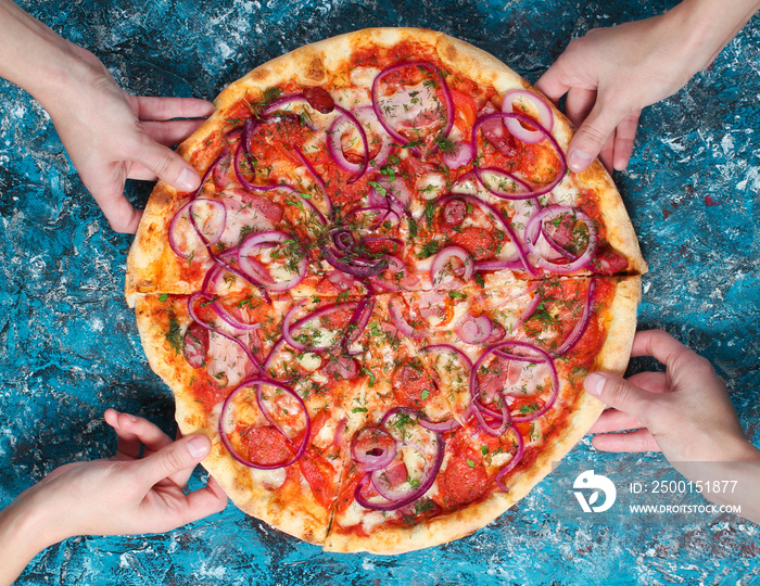 Hand takes a piece of homemade pizza on a blue concrete background.Company friends. Friendly snack. Top view.