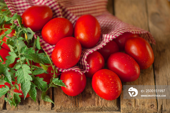 Long plum tomatoes with red checkered kitchen towel on wooden table. Heap of fresh tomatoes