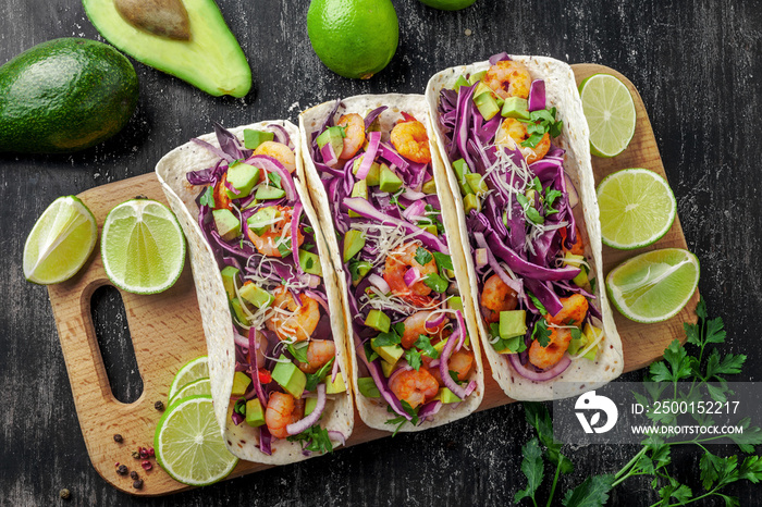 Delicious tacos with shrimps, avocado, onion and lime on a wooden board. Classic Tex-Mex cuisine meal. Top view shot, directly above.