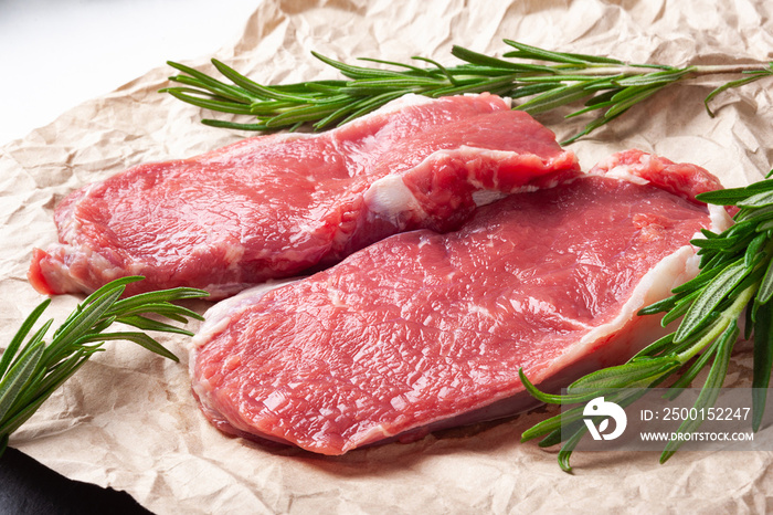 Raw meat . Two slices of fresh raw meat and rosemary on paper. Preparing meat for a barbecue.