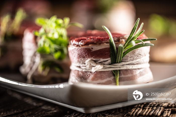 Raw steaks wrapped with bacon and fresh herbs on a plate and vintage wooden surface