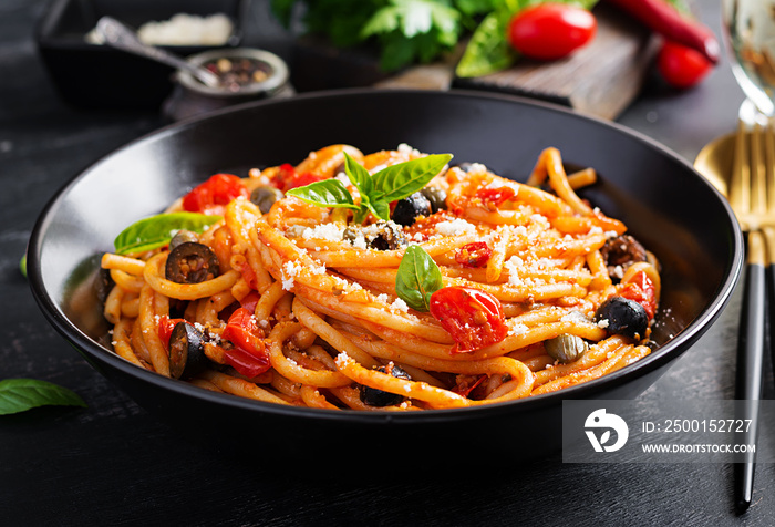 Spaghetti alla puttanesca - italian pasta dish with tomatoes, black olives, capers, anchovies and basil. Top view, flat lay