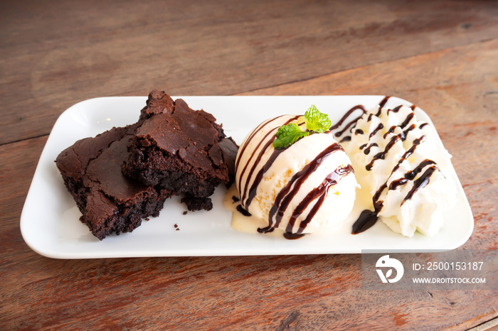 Homemade brownie served with vanilla ice cream and whipped cream on white plate. Sweet dessert with cocoa and coffee.