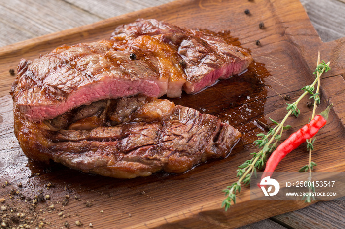 Cut Rib eye steak on wooden board, closeup. Rib eye steak on wooden board decorated with chili pepper