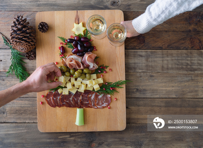 Spanish cheese and sausage board in the shape of a Christmas tree. Two people eating. Copy space.