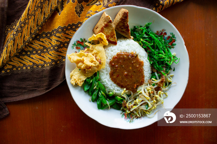 Nasi Pecel or sego pecel is Traditional Javanese rice dish of steamed rice with vegetable salad, peanut sauce, tempeh, tofu bean sprouts and crackers or peyek kacang.