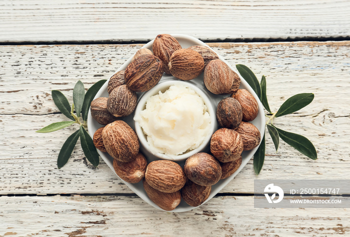 Bowl with shea butter and nuts on light wooden background