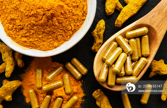 Turmeric powder and turmeric pills on a black concrete background