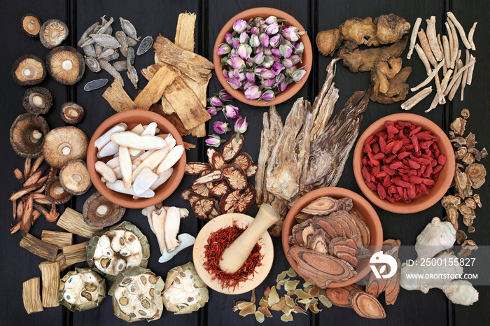 Chinese herbal medicine with herbs in terracotta bowls and loose with wooden mortar and pestle on dark wood background. Top view.