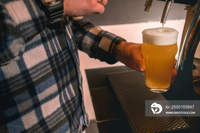 Bartender holding glass of beer under dispenser tap ready to serve to guest