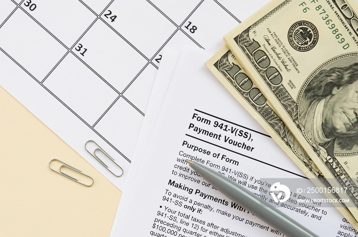 IRS Form 941-V Payment Voucher blank lies with pen and many hundred dollar bills on calendar page