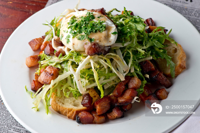 Salad. Frisee lettuce dress with olive oil and balsamic vinegar and topped with bacon lardons a fried egg and garnished with italian parsely and a toasted baguette. Served in a French Bistro.