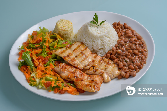 Brazilian healthy food. Plate with grilled chicken breast, accompanied by beans, rice, flour, vegetable salad in a white plate on the neutral table. Brazilian cuisine.