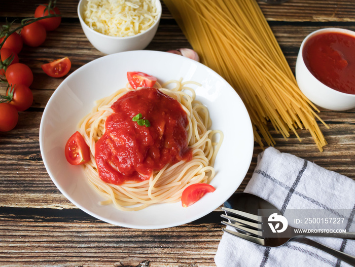 Spaghetti or pasta with tomato sauce, on a white plate on a dark wooden background with tomatoes.