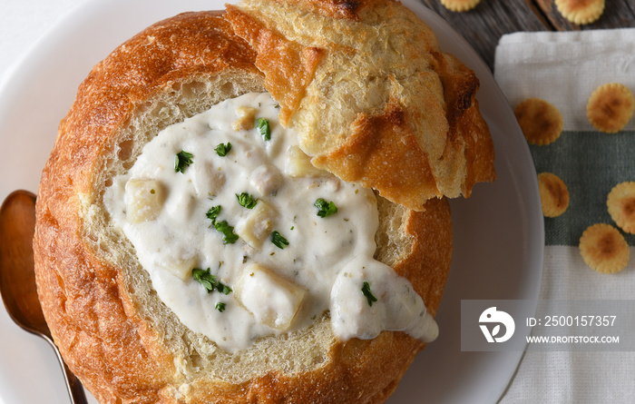 Overhead closeup of a bread bowl of New England Style Clam Chowder with napkin and oyster cracke