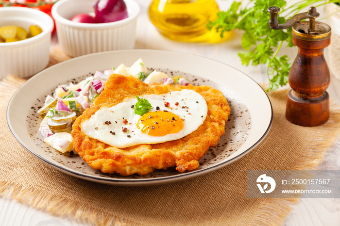 Viennese pork schnitzel with a fried egg. Served on potato salad. Natural wooden planks in the background.