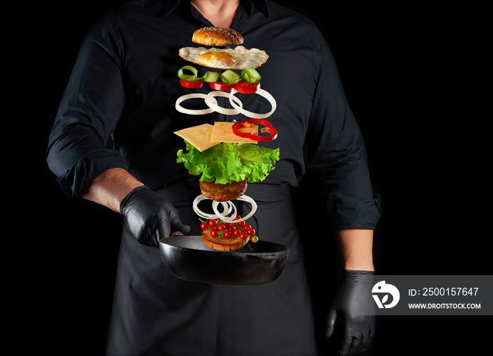 adult man in a black uniform holding a cast iron round frying pan with levitating cheeseburger ingredients