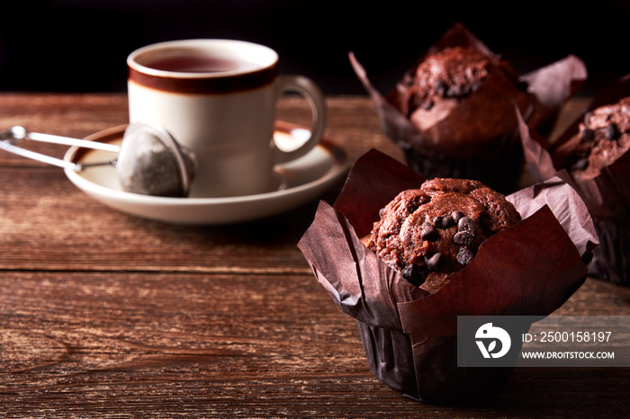 Still life with chocolate muffin and cup of tea on old wooden board table and with black background