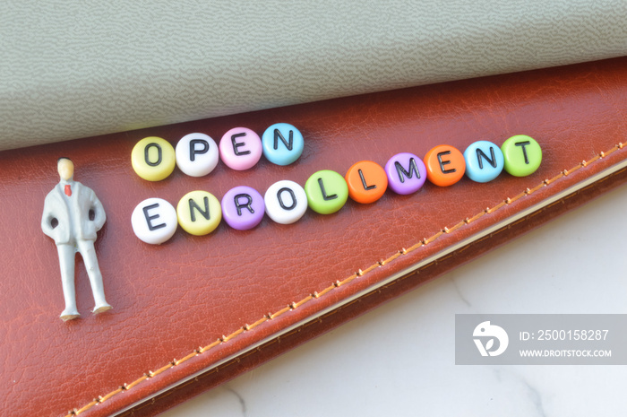 Selective focus of notebooks, miniature businessman and alphabet beads written with text OPEN ENROLLMENT. Business concept.