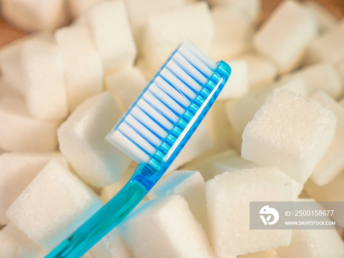 isolated conceptual still life image of toothbrush over massive pile of sugar cubes in dental care and oral hygiene concept as warning on sweet nutrition abuse